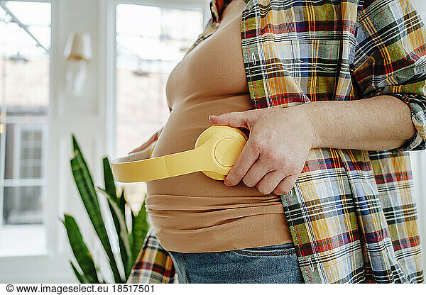Pregnant woman holding headphones on belly at home