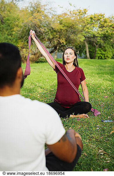 Pregnant woman holding resistance band sitting with man on lawn