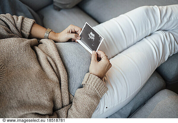 Pregnant woman holding ultrasound photo at home
