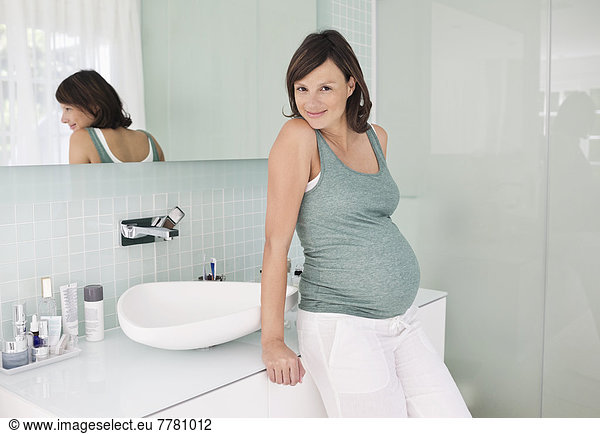 Pregnant woman leaning on bathroom sink