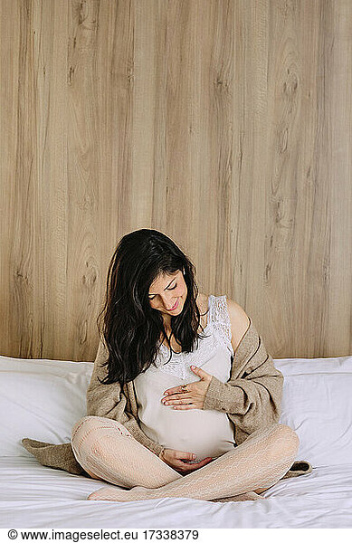 Pregnant woman looking at belly while sitting on bed