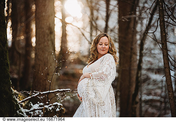Pregnant woman looking down in the woods in winter with golden light
