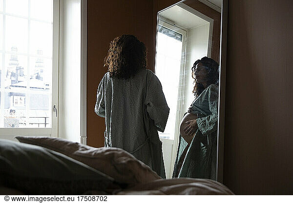 Pregnant woman looking in mirror at bedroom