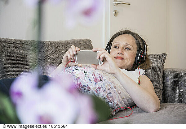 Pregnant woman lying on sofa and listening to music  Munich  Bavaria  Germany