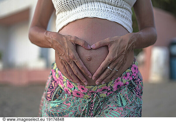 Pregnant woman making heart shape with hands on stomach