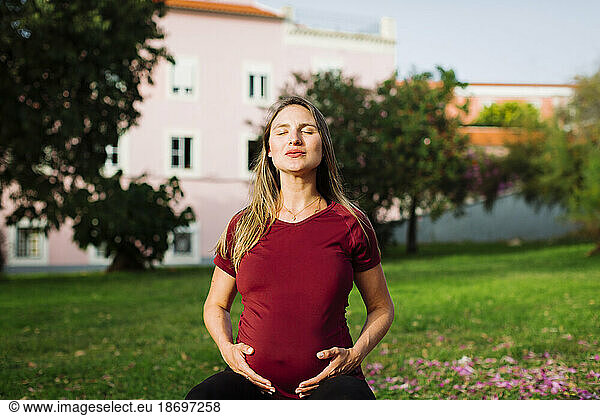 Pregnant woman meditating with hands on stomach on lawn
