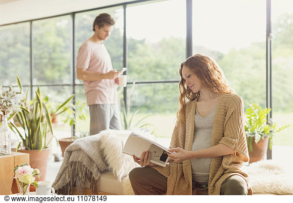 Pregnant woman reading book in living room