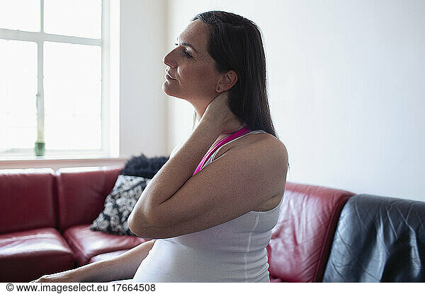 Pregnant woman rubbing neck on sofa