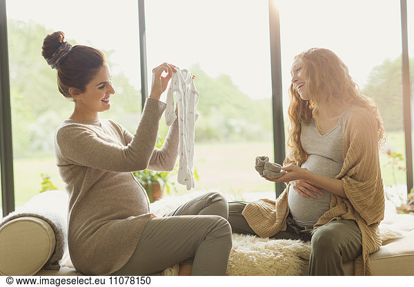 Pregnant woman showing baby clothing to friend