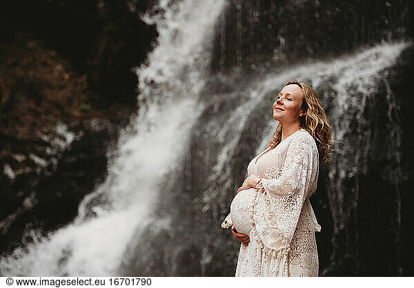 Pregnant woman smiling outside on a cold winter day by a waterfall