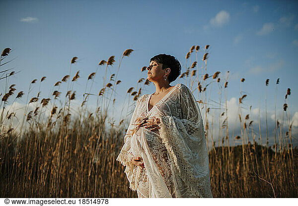 Pregnant woman standing in field at sunset