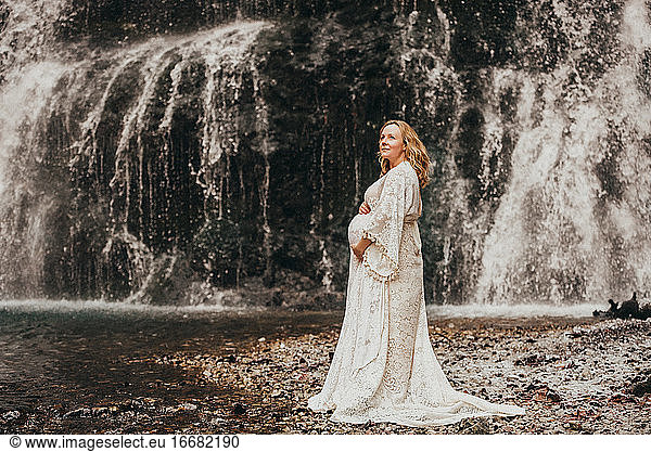 Pregnant woman standing in front of waterfall in winter touching belly