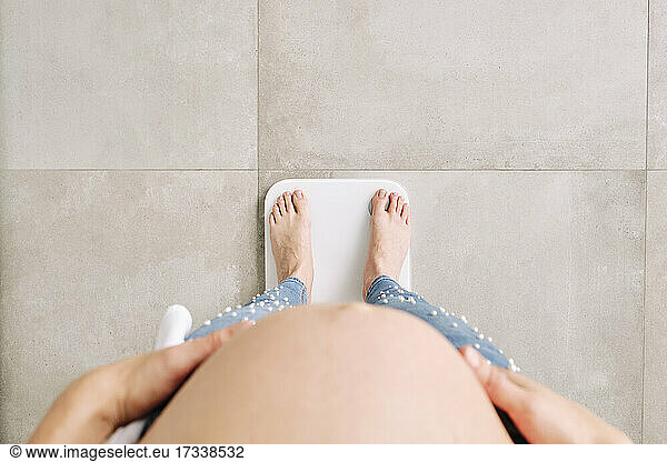 Pregnant woman standing on weighing scale at home