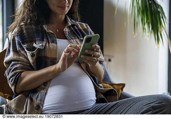 Pregnant woman texting on mobile phone at home