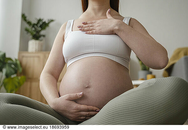 Pregnant woman touching belly sitting cross-legged at home