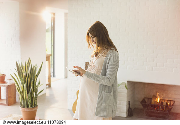 Pregnant woman using digital tablet near fireplace in living room