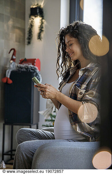 Pregnant woman using smart phone sitting at home