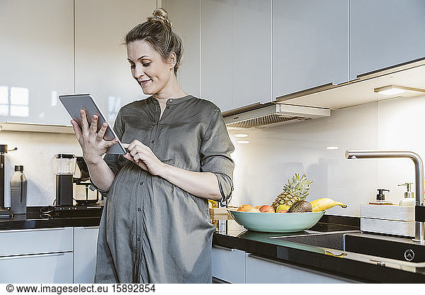 Pregnant woman using tablet in kitchen at home