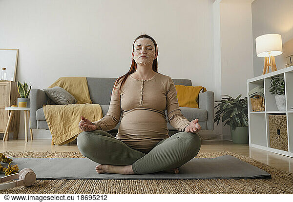 Pregnant woman with cosmetic mask meditating at home