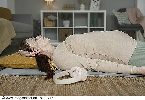 Pregnant woman with face mask lying on exercise mat at home
