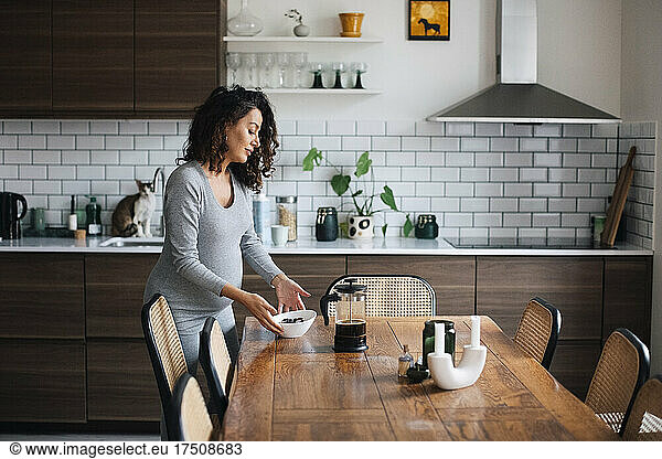 Pregnant woman with food bowl at dining table in kitchen