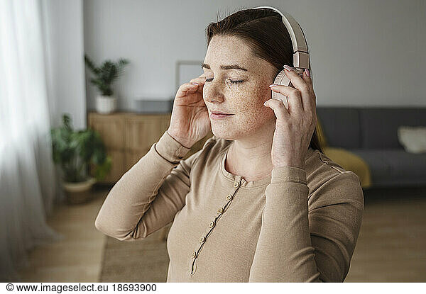 Pregnant woman with freckles adjusting headphones at home