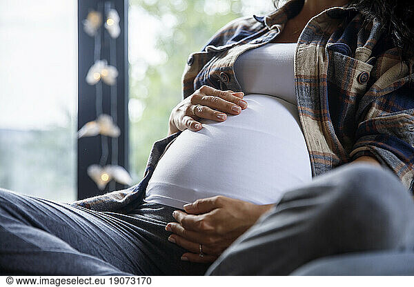 Pregnant woman with hands on stomach at home