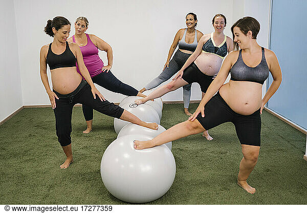 Pregnant woman with leg on fitness ball standing at yoga studio
