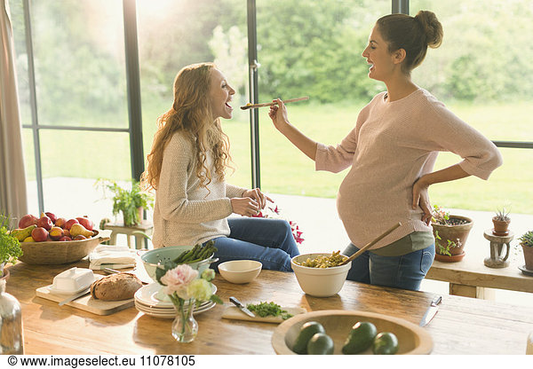 Pregnant women cooking and tasting food at table