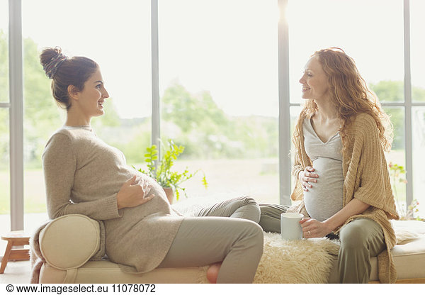 Pregnant women drinking tea and talking in living room