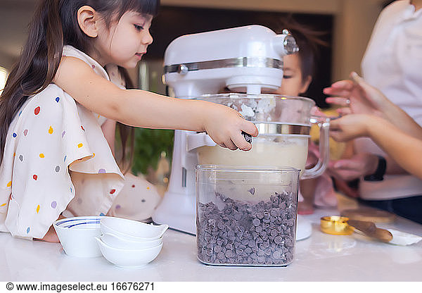 Preschooler baking with her family  adding chocolate chips to mixer.