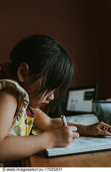 Preschooler coloring at home with laptop open