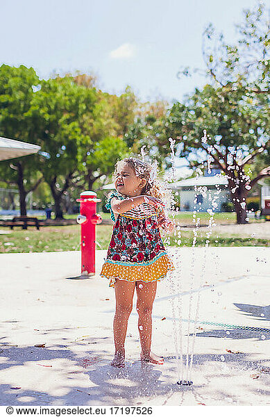 Preschooler girl playing with water at a public playground.