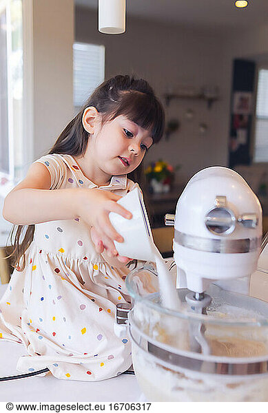 Preschooler pouring sugar into mixer bowl.