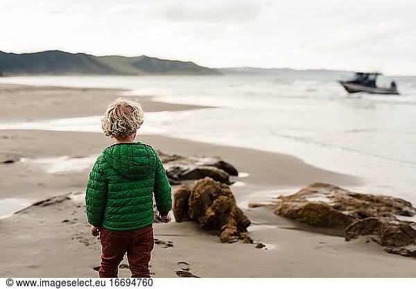 Preschooler watching boat at beach in New Zealand