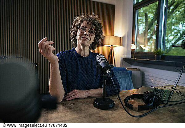 Presenter wearing eyeglasses sitting with microphone at desk in recording studio