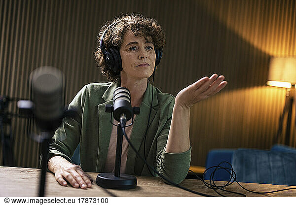 Presenter wearing headset gesturing sitting with microphone at radio station