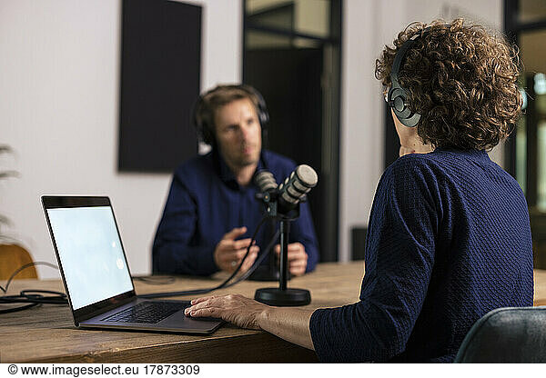 Presenter wearing headset interviewing guest in recording studio