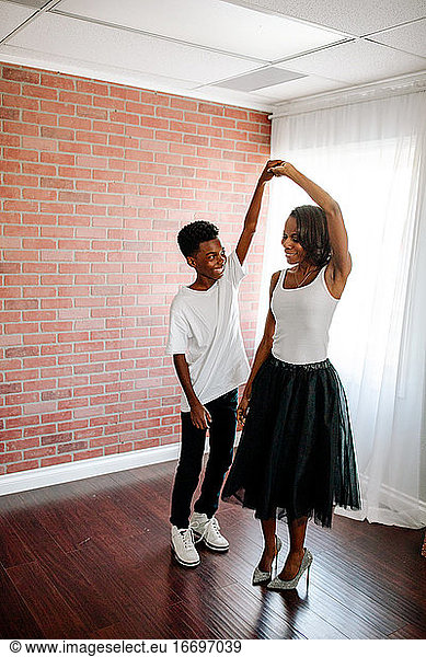 Preteen black boy dancing with mom in tulle skirt and spike heels