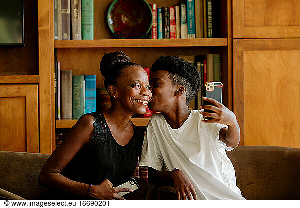 Preteen Black boy takes selfie while kissing smiling mother
