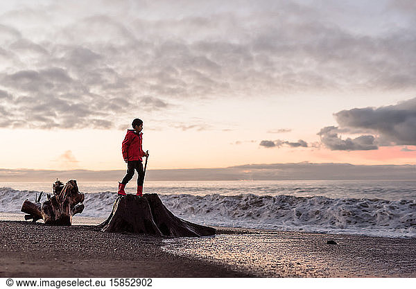 Preteen boy climbing on tree stump at beach