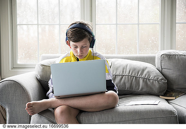 Preteen Boy Wearing Headphones Works on Laptop for Virtual School