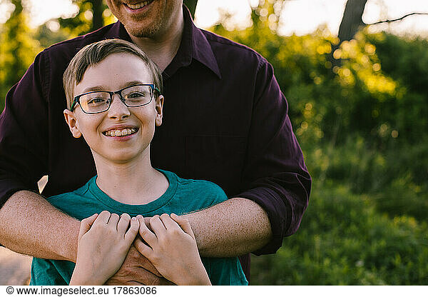 Preteen boy with glasses has happy smile while Dad hugs him