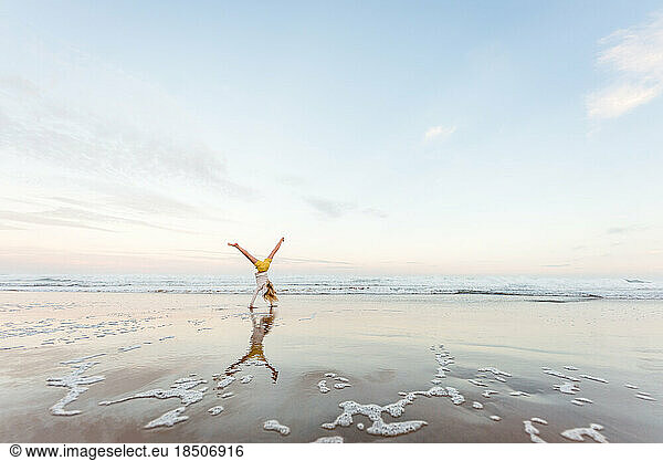 Preteen girl doing a cartwheel at beach with reflection
