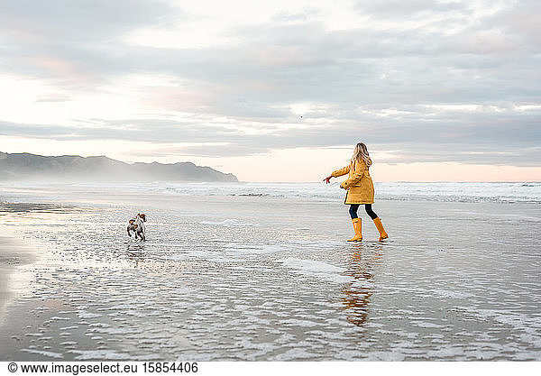 Preteen girl playing with dog at beach in New Zealand