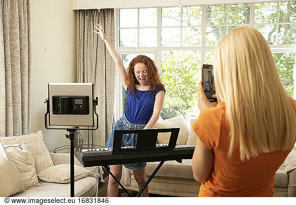 Preteen girl with smart phone filming friend playing keyboard piano