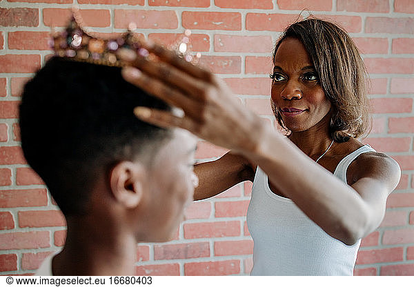 Pretty black mom placing crown on preteen son