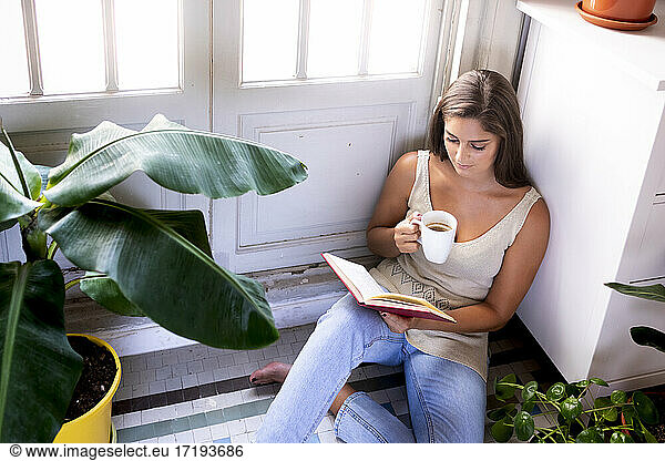 Pretty girl read a book and take coffee at home sitting on the floor