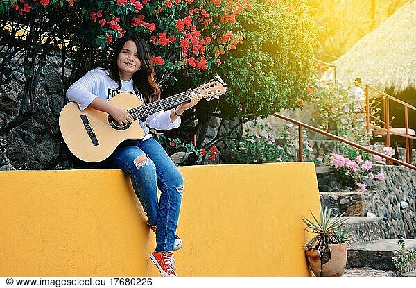 Pretty smiling girl sitting playing guitar outdoors  Portrait of smiling girl playing guitar  Lifestyle of girl playing guitar outdoors