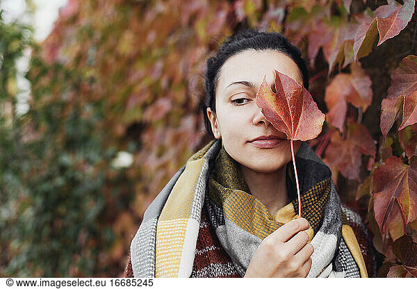 Pretty woman covering her face with a red leaf and looking aside
